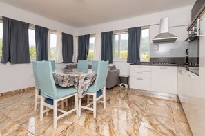 A modern kitchen with a dining area, marble flooring, and large windows with curtains.