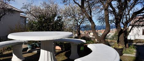 A white outdoor table and bench set in a garden with a view of a town and a tree with blossoms.
