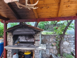 Ein rustikaler, steinerner Außenofen mit Schornstein, umgeben von einer Holzkonstruktion und Steinmauern.