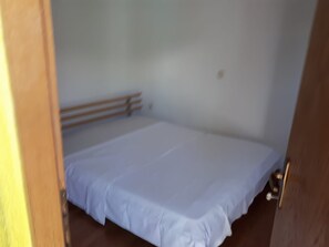 Ein Zimmer mit einem Bett, einem Holzkopfende, einer Tür und einem Lichtschalter an der Wand.