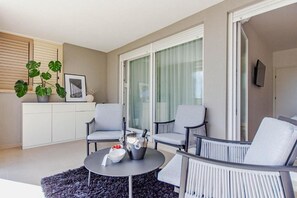 A modern living room with a round coffee table, two grey armchairs, a white cabinet, a large window with curtains, and a potted plant. - Apartment Sea View Garden (Split)