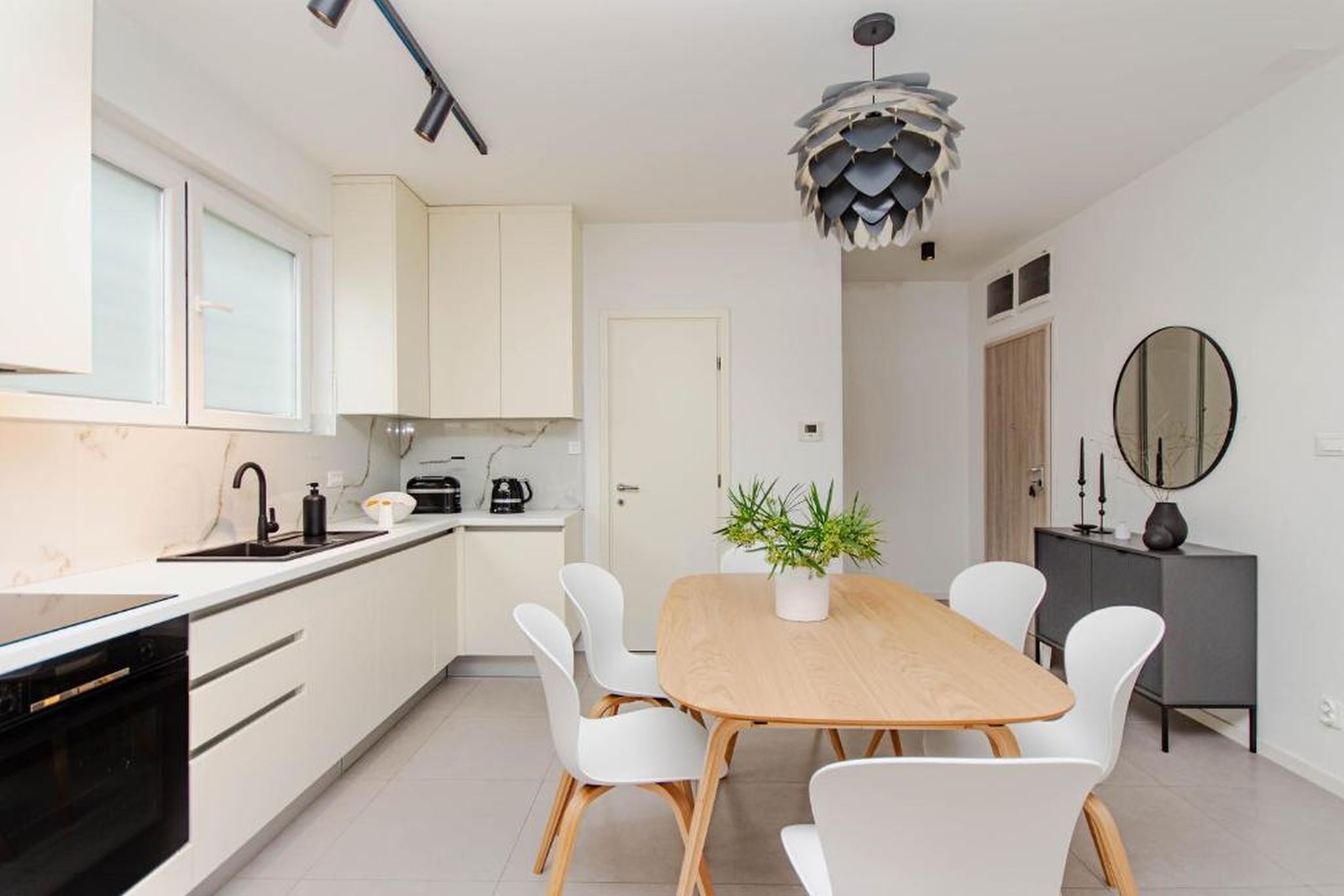 Una cocina moderna con armarios blancos, un horno negro y una mesa de comedor de madera con sillas blancas.