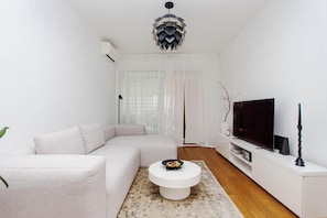 A modern living room with a sectional sofa, a round coffee table, a flat-screen TV, and a decorative ceiling light. - Apartment Sea View Garden (Split)