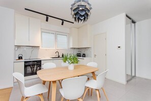 A modern kitchen with white cabinets, a wooden dining table, and white chairs. - Apartment Sea View Garden (Split)
