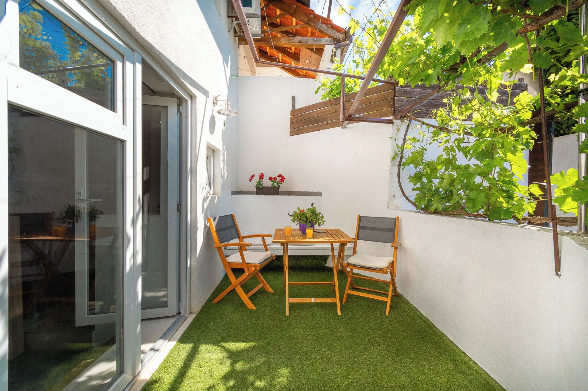 A small patio with a table and chairs, a potted plant, and a wooden pergola.