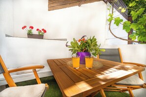 Ein Holztisch mit zwei Gläsern Orangensaft, einem violetten Topf mit Grünpflanzen und einem weiß gepolsterten Stuhl.