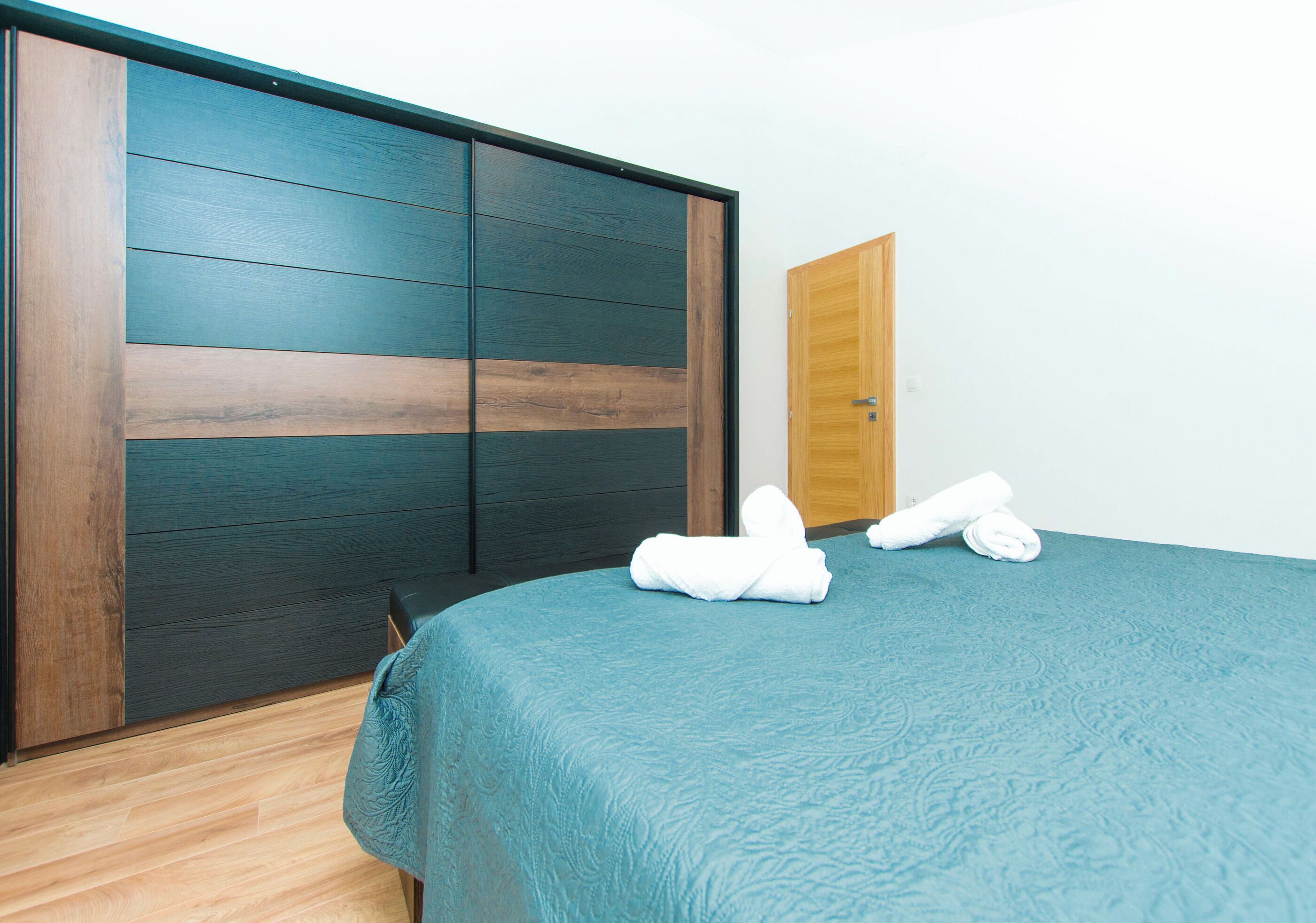 A room with a bed, a wooden door, and a sliding wardrobe.