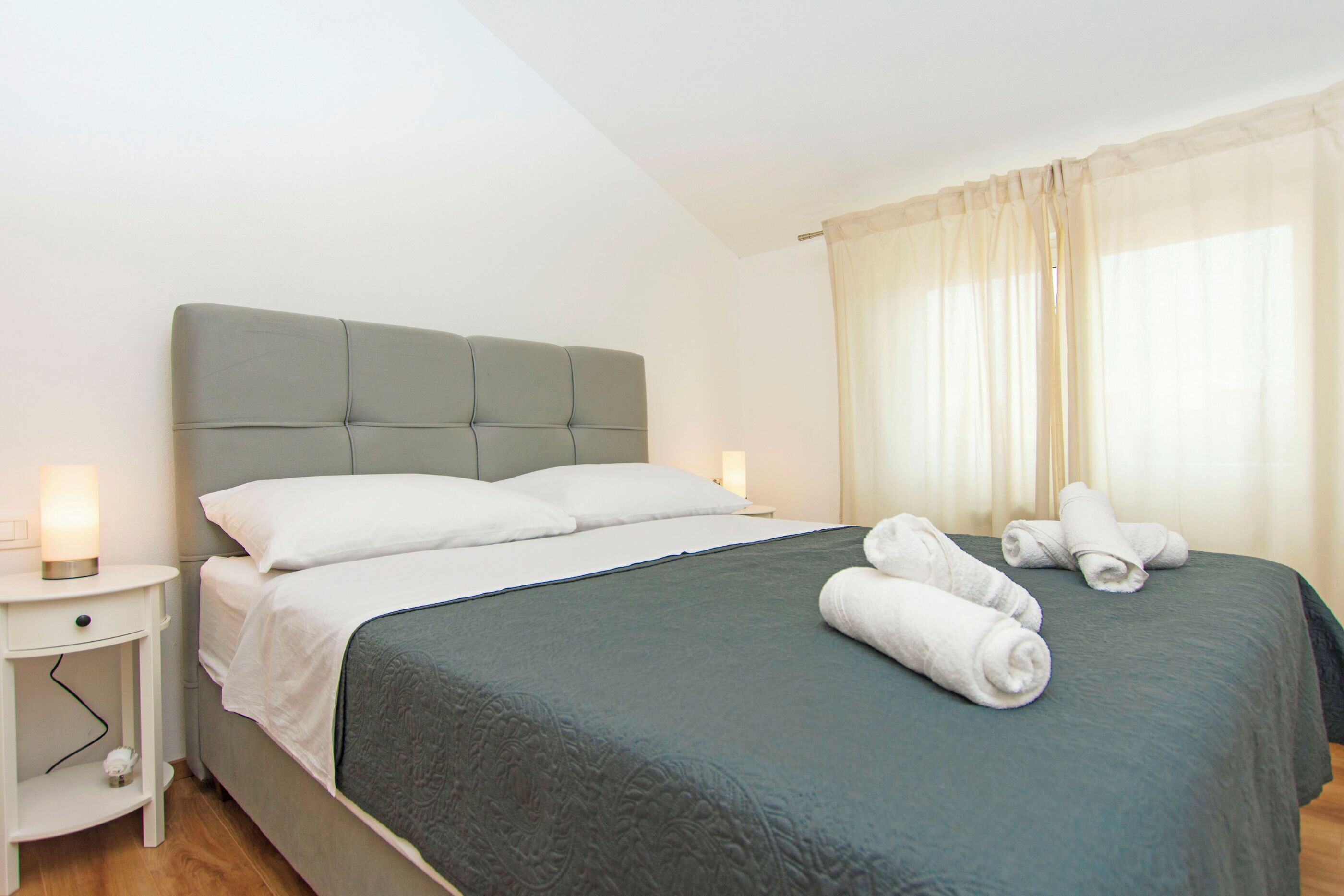 A neatly made bed with a green bedspread, white pillows, and rolled towels on the bed.