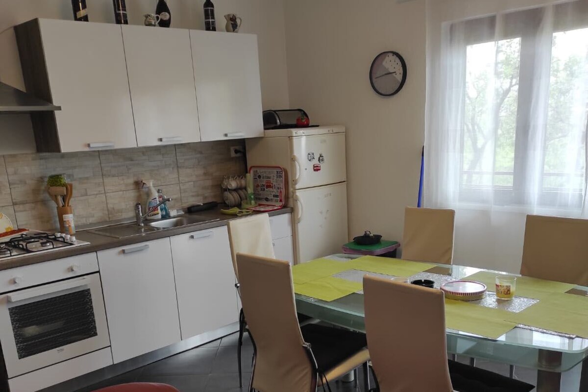 A modern kitchen with white cabinets, a dining table with chairs, a red leather couch, and a window with curtains.