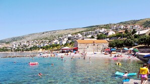 A coastal town with clear waters, a beach, and buildings on a hillside. - Apartments Nina i Harry (Senj)