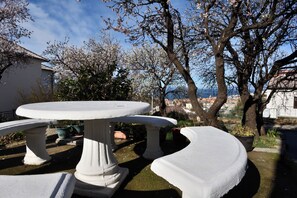 Ein weißes Tisch- und Bänkchen-Set im Garten mit Blick auf eine Stadt und einen Baum in voller Blüte.