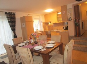 A dining area with a table set for four, a kitchen in the background, and a staircase leading to an upper floor. - House Mira (Buje)