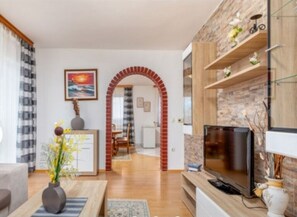 A living room with a TV, a fireplace, and a dining area in the background. - House Mira (Buje)