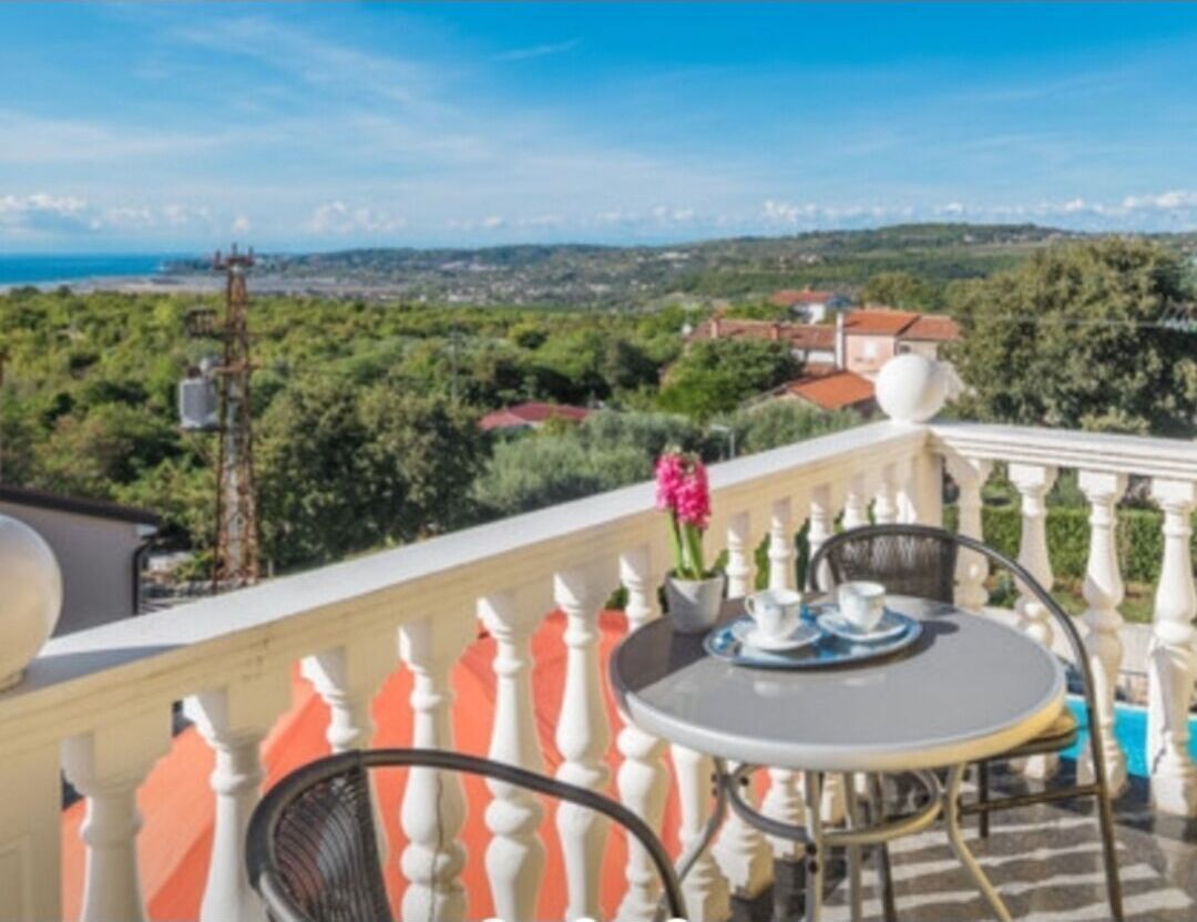 A balcony with a table and chairs, overlooking a scenic landscape with trees and buildings.