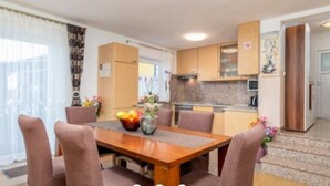 Een eetruimte met een houten tafel en stoelen, een keuken met houten kastjes, en een koelkast.