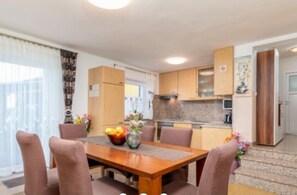 A dining area with a wooden table and chairs, a kitchen with wooden cabinets, and a refrigerator. - House Mira (Buje)