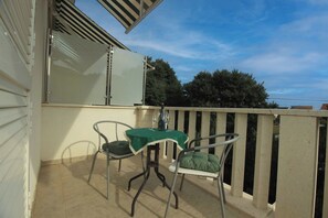 Ein Balkon mit Tisch, Stühlen, einer Glastür und Blick auf Bäume.