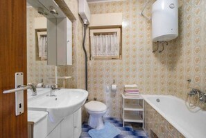 A bathroom with a sink, toilet, and bathtub, with patterned wallpaper and a mirror above the sink. - Apartments Merica (Sibenik)