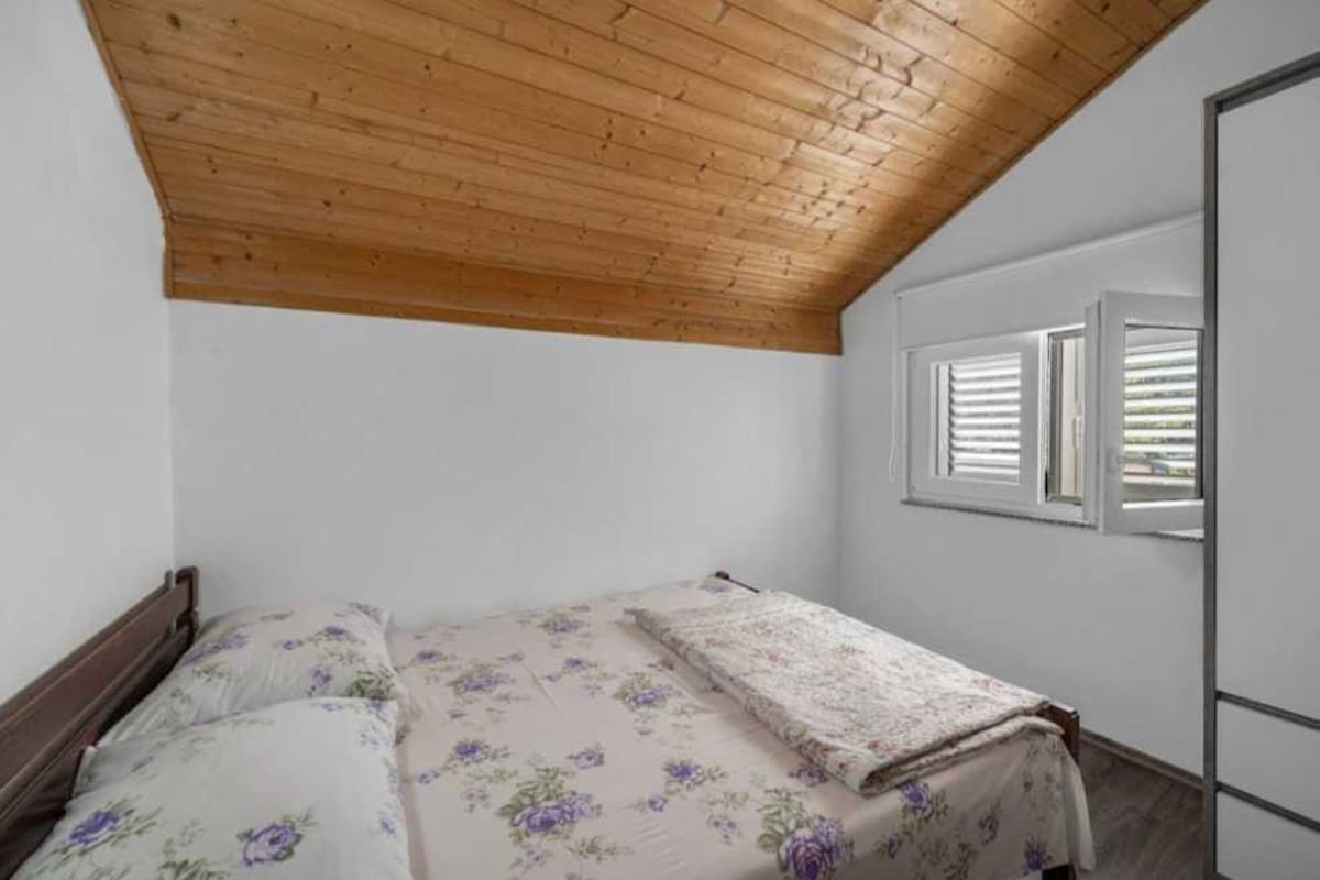 A bedroom with a wooden ceiling, a bed with floral bedding, and a window with shutters.