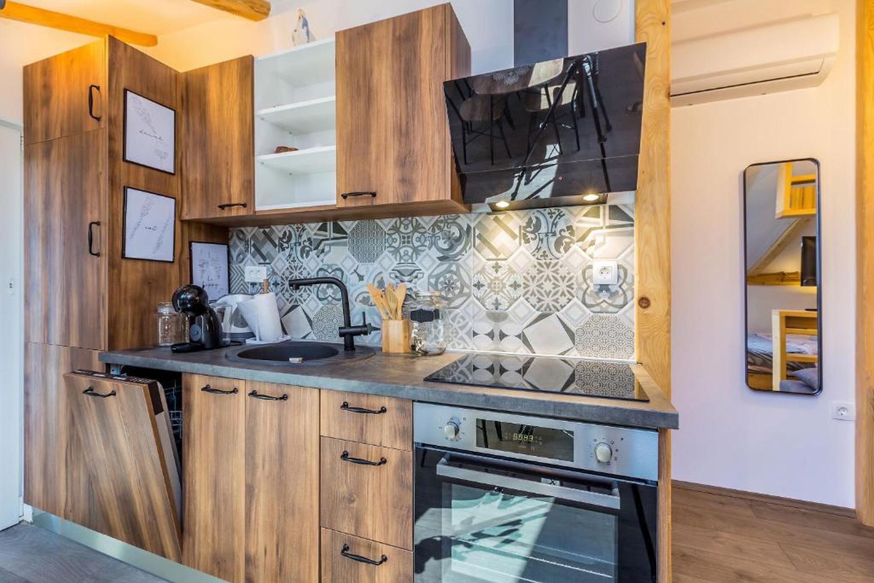 A modern kitchen with wooden cabinets, a built-in oven, and a backsplash with geometric patterns.