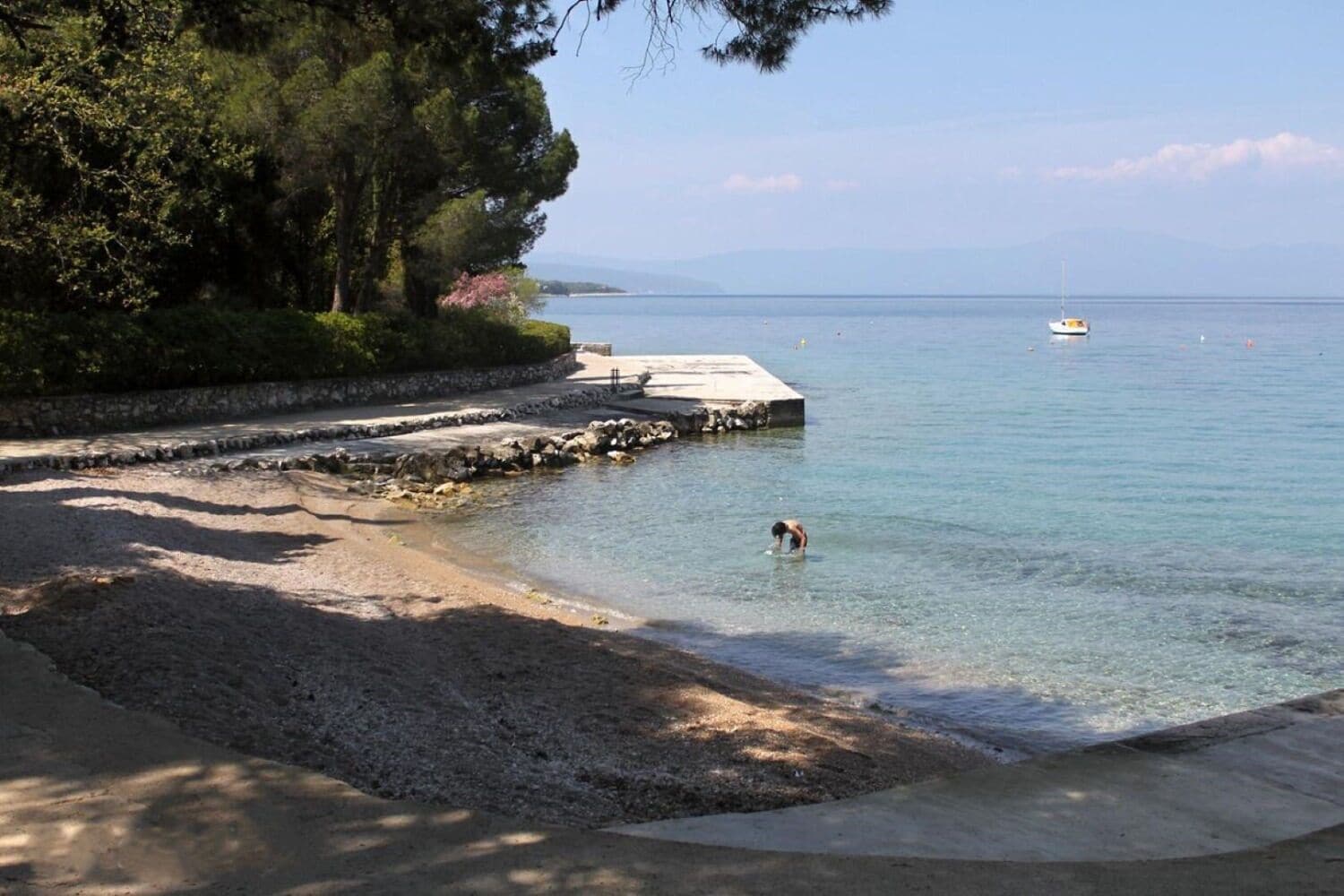 A beach with clear water, a dock, and a person swimming.