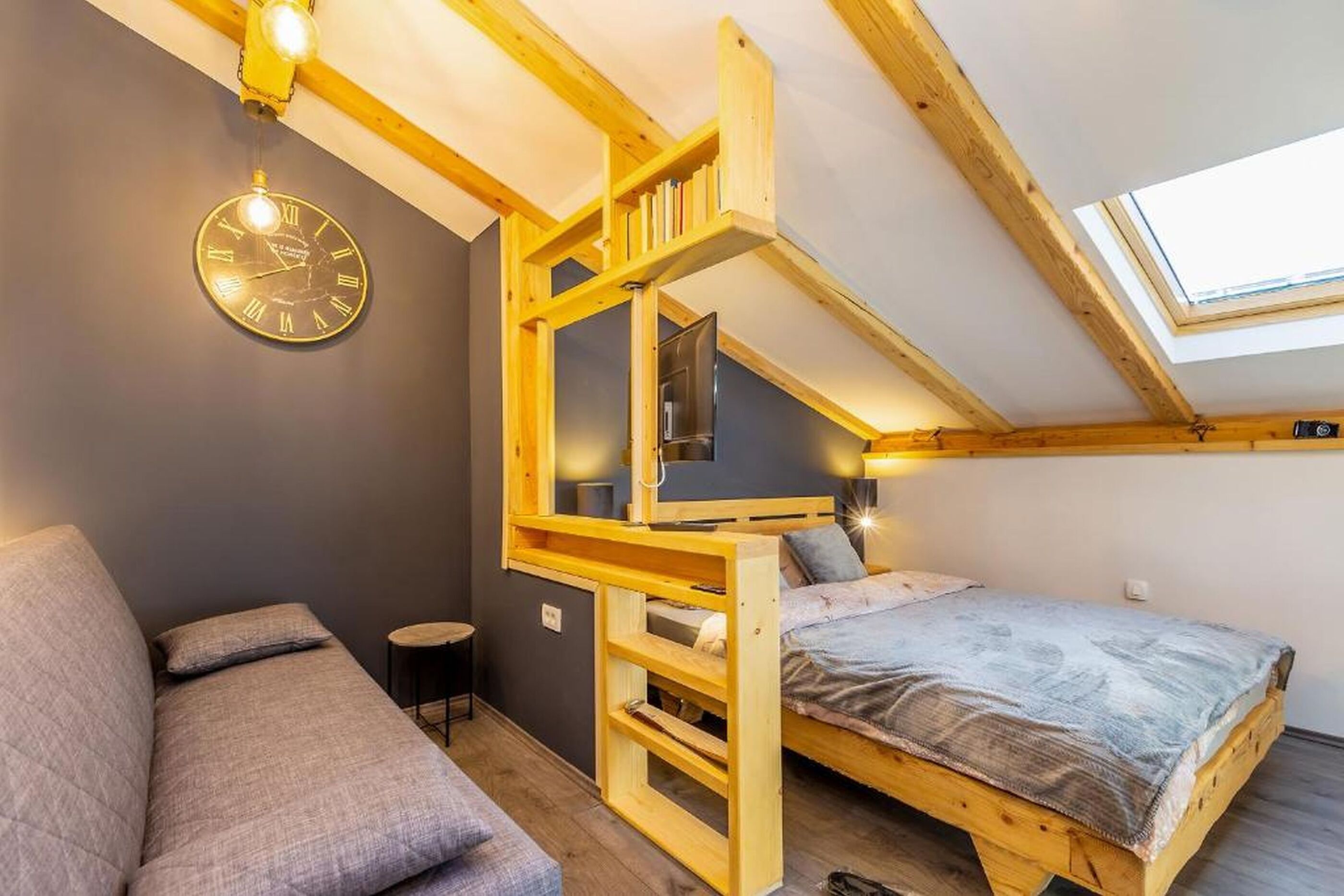 A loft-style bedroom with a bunk bed, a sofa, a clock, and a skylight.