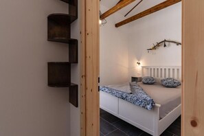 Un dormitorio con cama blanca, estantes de madera oscura, un radiador blanco y una decoración con ramas.