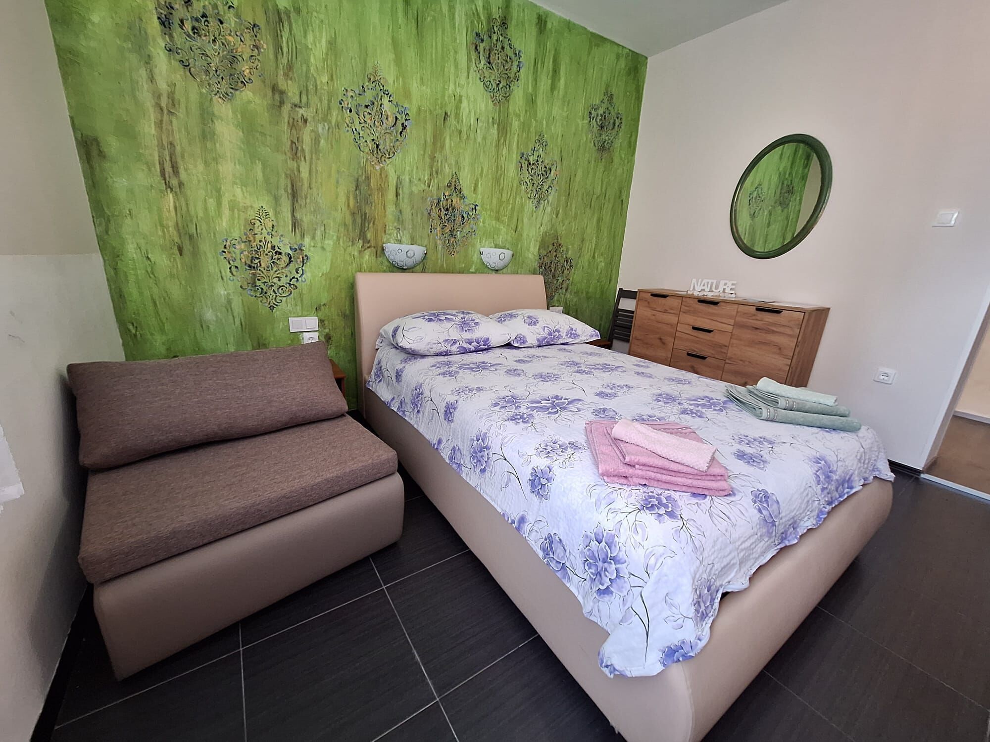 Ein Schlafzimmer mit einem Bett, einem Sofa, einer Kommode und einer grünen Wand mit dekorativen Mustern.