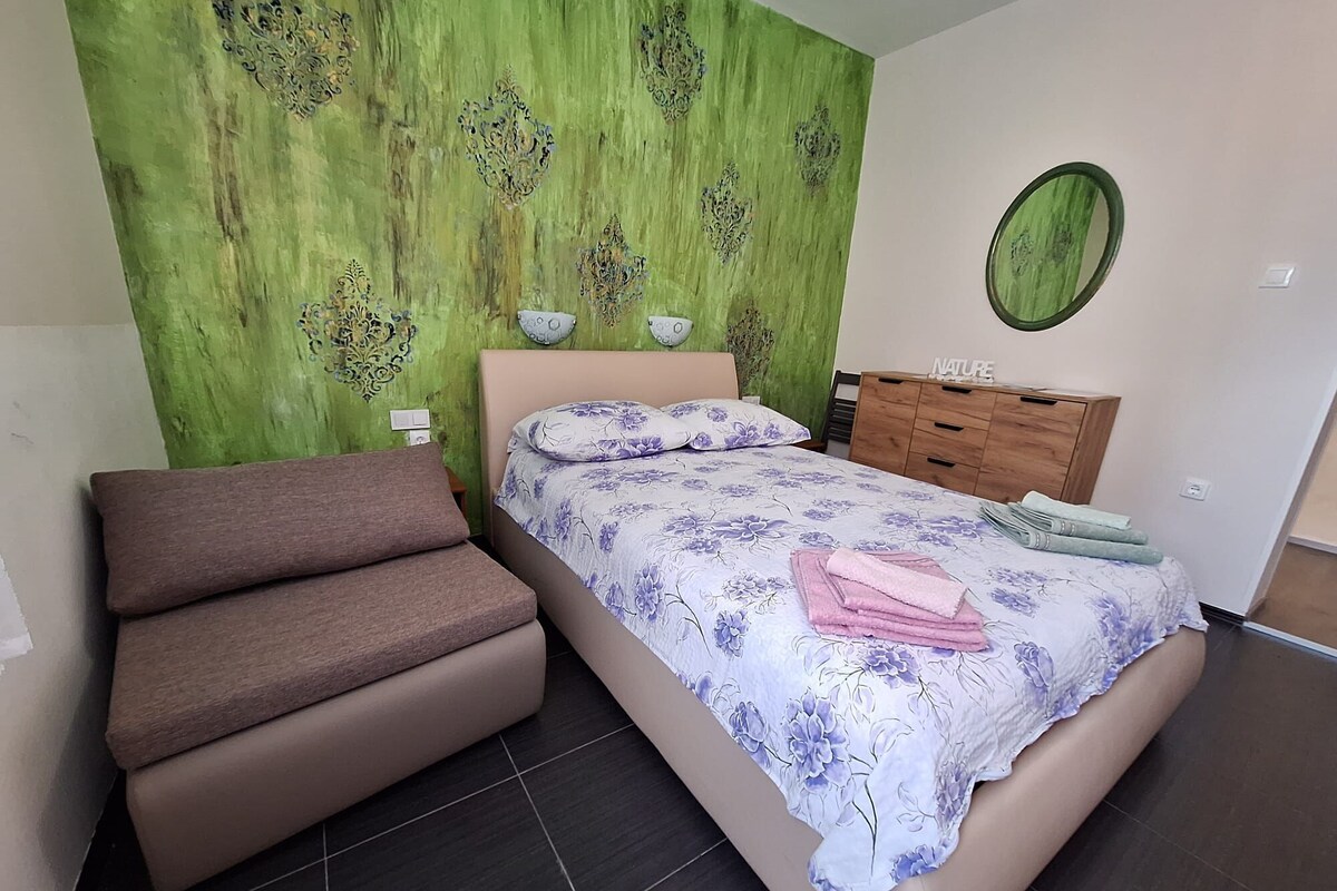 Ein Schlafzimmer mit einem Bett, einem Sofa, einer Kommode und einer grünen Wand mit dekorativen Mustern.