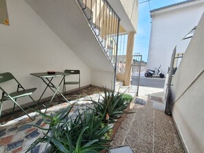 Ein kleiner Außenbereich mit Tisch und Stühlen, eine Treppe und Blick auf eine Straße, auf der ein Roller steht.