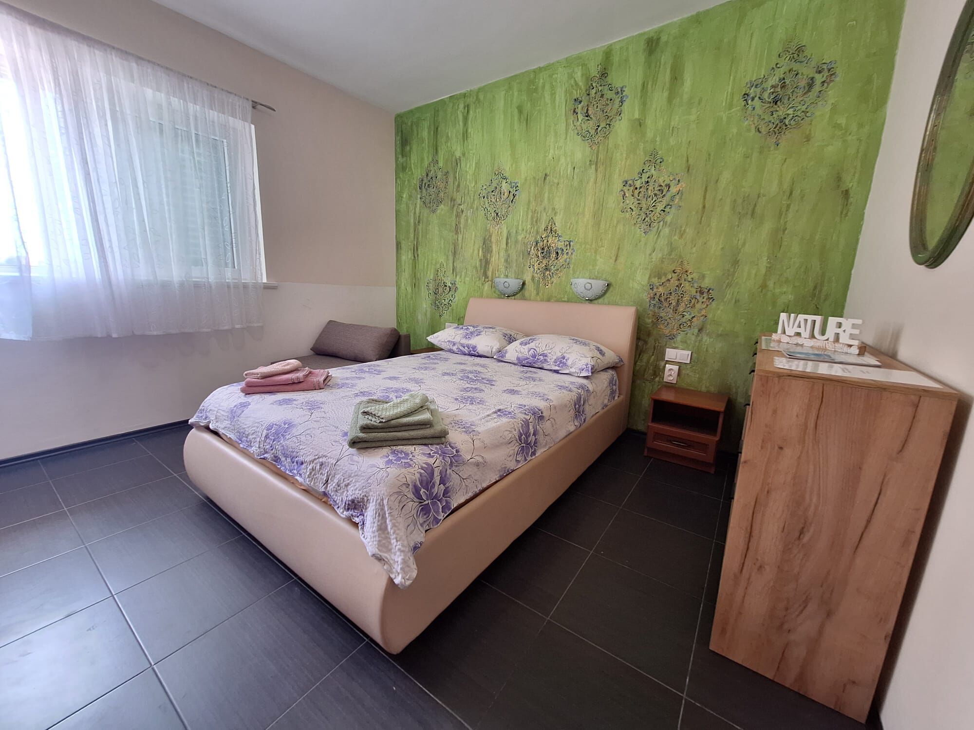 A bedroom with a bed, a nightstand, a wooden cabinet, and a green wall with decorative elements.