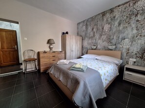 Ein Schlafzimmer mit einem Bett, einem Holzschrank, einem Stuhl, einem Nachttisch und einer Lampe.