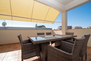 Eine überdachte Terrasse mit Tisch und Stühlen, Blick zum Himmel und Gebäuden im Hintergrund.