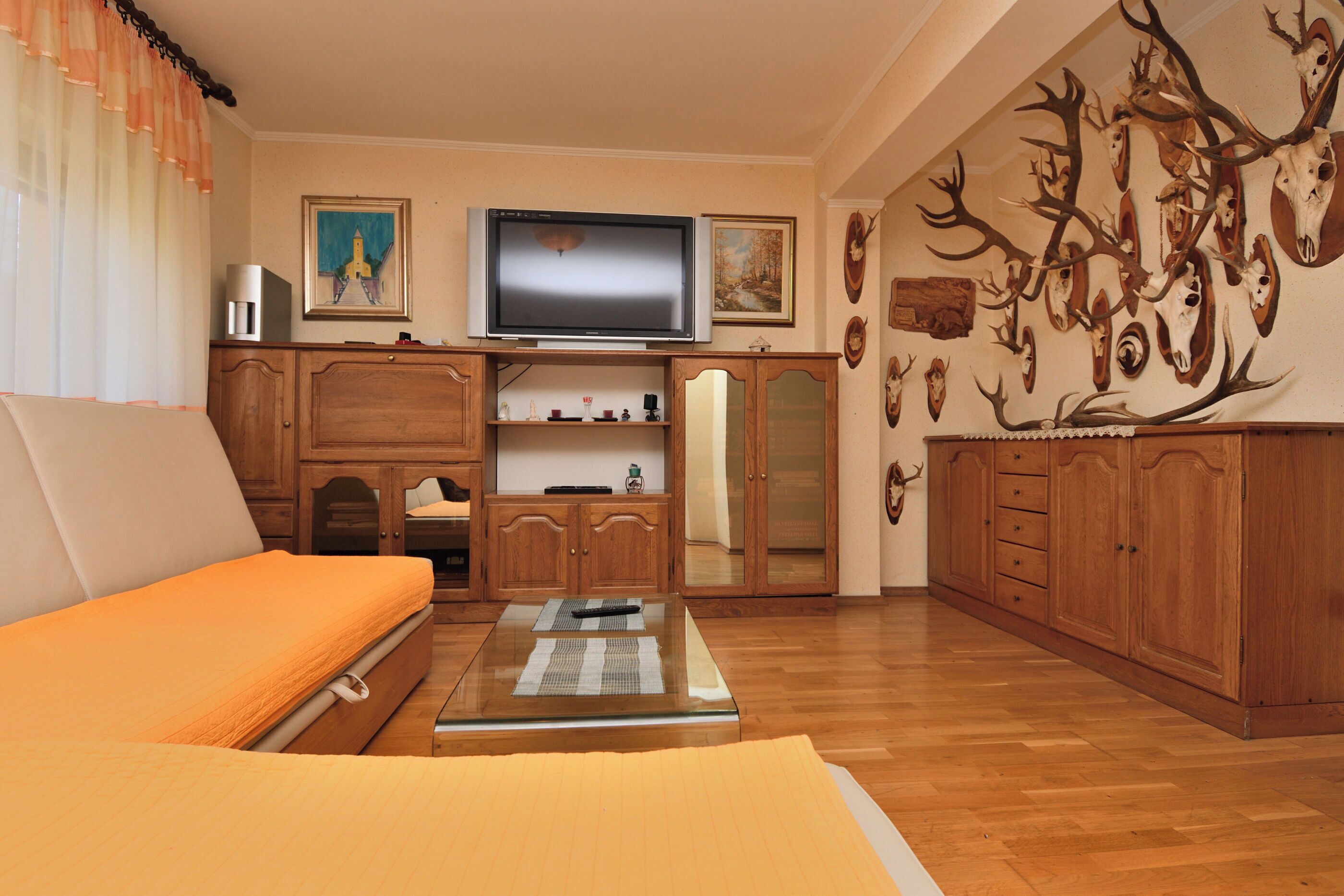 Ein Zimmer mit einem Bett, einem Fernseher, Holzschränken und einer Wand mit montierten Tierkopfschädeln.