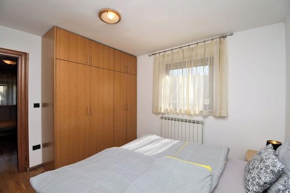A bedroom with a bed, wooden wardrobe, and a window with curtains. - Apartment Tadey (Fuzine)