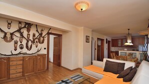 Una sala de estar con un mueble de madera, una mesa de centro de vidrio, un sofá y un ciervo montado en la pared.
