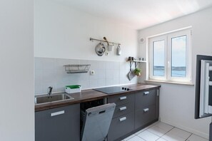 Eine moderne Küche mit grauen Schränken, einer Holz Arbeitsplatte, einem Fenster mit Blick und einem Hängegestell mit Küchenutensilien.