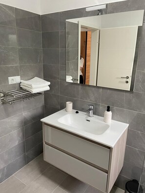 A modern bathroom with a white sink, a towel rack, a mirror, and a door. - Apartment Maslina Sea View (Preko)