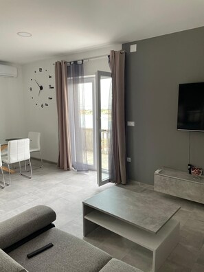 A modern living room with a sofa, a coffee table, a TV, and a dining area with a table and chairs. - Apartment Maslina Sea View (Preko)