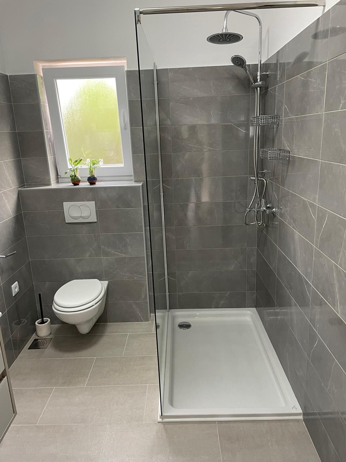 Un baño moderno con ducha de vidrio, inodoro y ventana con plantas.