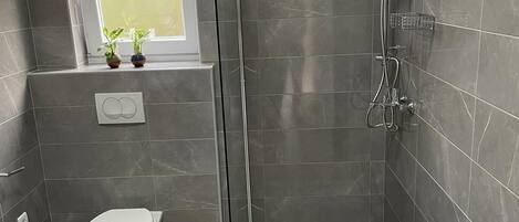 Un baño moderno con ducha de vidrio, inodoro y ventana con plantas.