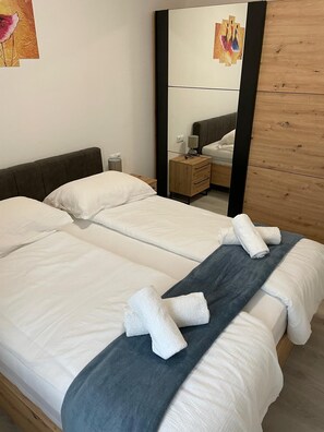 A double bed with white linens and a grey blanket, a wooden nightstand with a lamp, and a mirror reflecting the room. - Apartment Maslina Sea View (Preko)