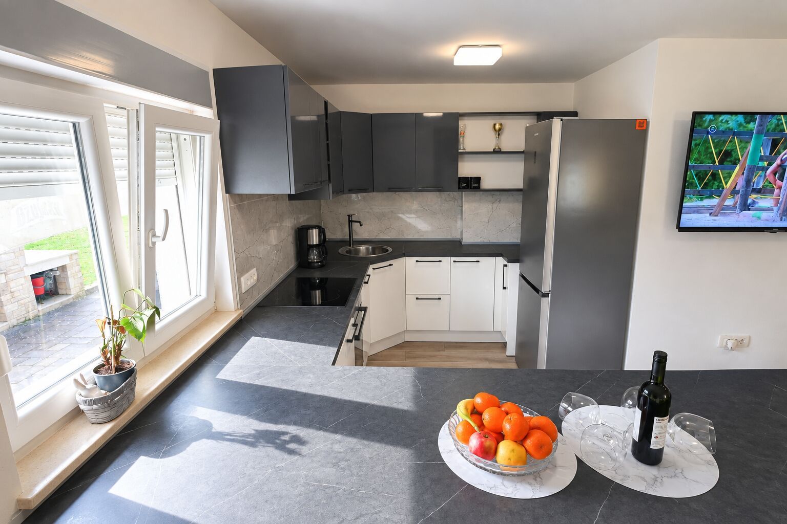 A modern kitchen with a built-in oven, a coffee maker, and a sink. There is a fruit bowl on the counter and a bottle of wine.