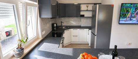 A modern kitchen with a built-in oven, a coffee maker, and a sink. There is a fruit bowl on the counter and a bottle of wine.