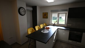 A compact kitchen with a dining area, a clock, and a window with blinds. - House Ivana (Pula)