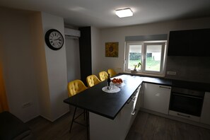 A compact kitchen with a dining area, a clock, and a window with blinds. - House Ivana (Pula)