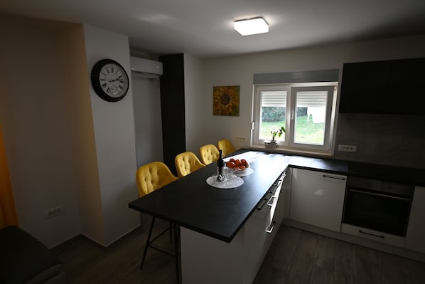 A compact kitchen with a dining area, a clock, and a window with blinds. - House Ivana (Pula)