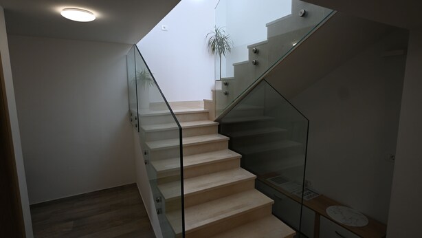 A modern staircase with glass railings, a wooden floor, and a small plant in the background. - House Ivana (Pula)