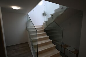 A modern staircase with glass railings, a wooden floor, and a small plant in the background. - House Ivana (Pula)