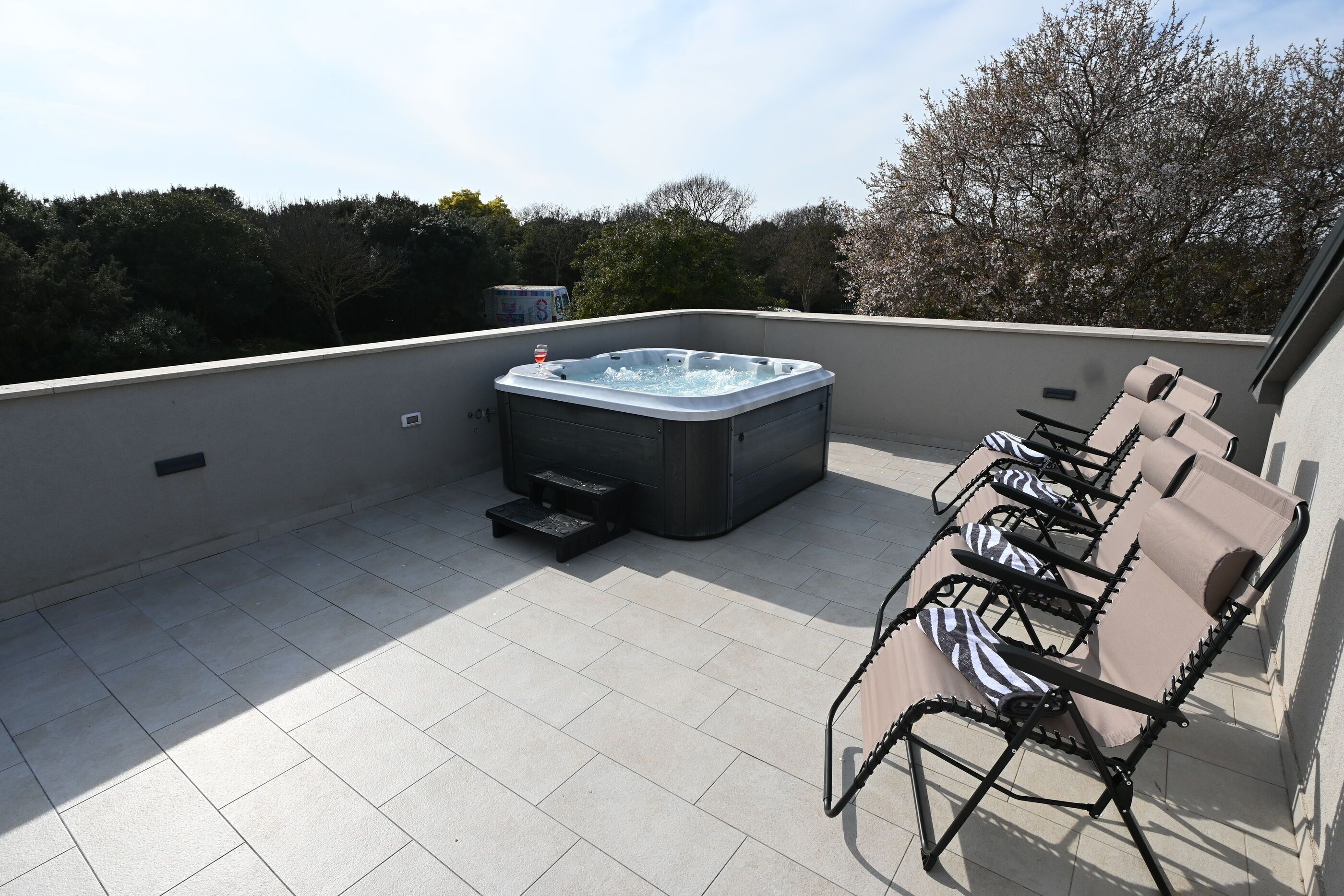 Eine Dachterrasse mit Whirlpool, Sitzgelegenheiten im Freien und Blick auf Bäume.